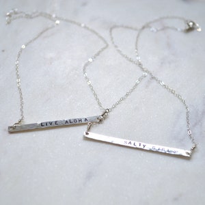 May include: Two silver necklaces with hammered bar pendants. The top pendant says "LIVE ALOHA" and the bottom pendant says "SALTY GIRL".
