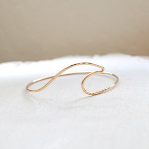 May include: A gold-toned wave-shaped bracelet. The bracelet is made of thin metal and has a hammered texture.