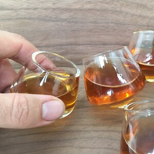 May include: Four clear glass shot glasses filled with amber liquid, sitting on a wooden surface.