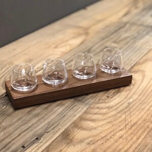 May include: A wooden tray with four small clear glass cups. The tray is made of dark wood and has a smooth finish.