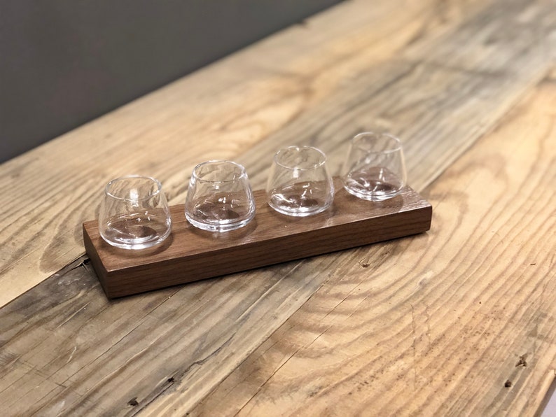 May include: A wooden tray with four small clear glass cups. The tray is made of dark wood and has a smooth finish.