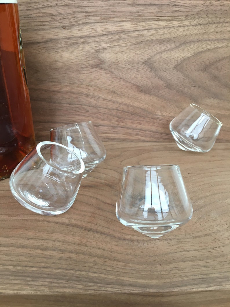 May include: Four clear glass shot glasses on a wooden surface. The glasses are round and have a wide base.