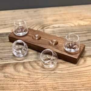 May include: A wooden serving tray with four small, clear glass cups. The tray has four indentations for the cups to sit in.
