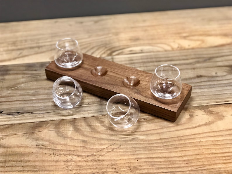 May include: A wooden serving tray with four small, clear glass cups. The tray has four indentations for the cups to sit in.