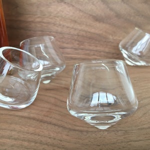 May include: Four clear glass shot glasses with a unique, rounded, and slightly tilted design. The glasses are arranged on a wooden surface.