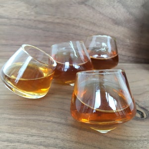 May include: Four clear glass shot glasses filled with a golden brown liquid, sitting on a wooden surface.
