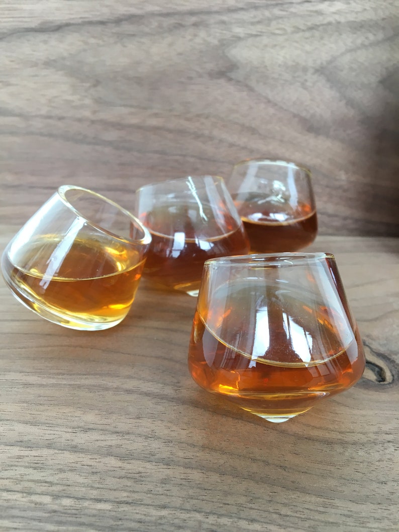 May include: Four clear glass shot glasses filled with a golden brown liquid, sitting on a wooden surface.