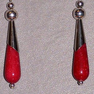 May include: A pair of silver dangle earrings with red gemstone drops. The earrings have a silver teardrop shape with a red gemstone inside.