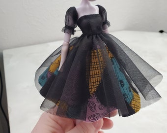 Puede incluir: Un vestido de tul negro con un corpiño negro y una tela estampada debajo. El vestido tiene mangas cortas y abullonadas.