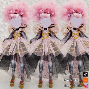 May include: Three dolls with pink afro wigs, floral headbands, and heart-shaped faces. They wear black and pink dresses with gold accents, black chokers, and gold shoes. The dolls have decorative wings and patterned stockings. The image includes social media handles.