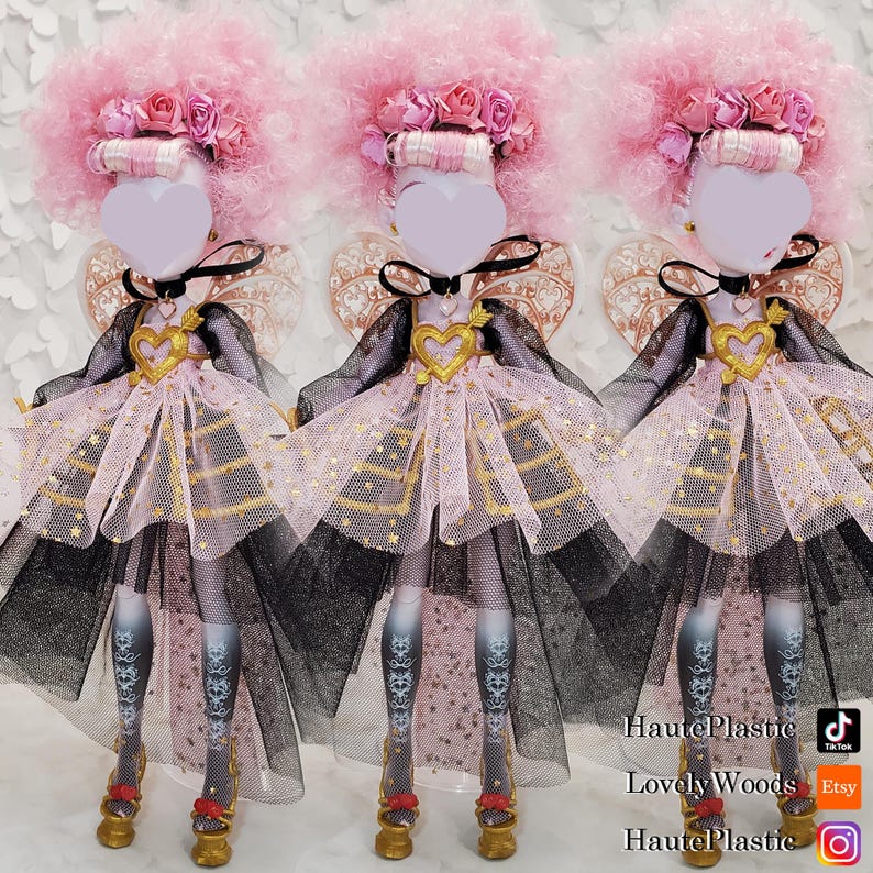 May include: Three dolls with pink afro wigs, floral headbands, and heart-shaped faces. They wear black and pink dresses with gold accents, black chokers, and gold shoes. The dolls have decorative wings and patterned stockings. The image includes social media handles.