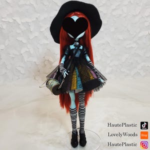 May include: A blue and black doll with red hair wearing a black and white striped dress and a black witch hat. The doll is holding a spool of thread and a black bag.