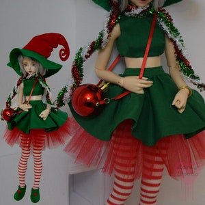 May include: Two dolls dressed in Christmas elf costumes. The outfits include green crop tops and skirts, red and white striped leggings, and red tulle underskirts. Each doll wears a red and green elf hat and carries a red ornament purse. Tinsel accents the outfits.