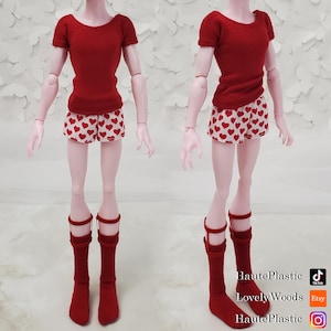 May include: A doll outfit consisting of a short-sleeved red knit top, white shorts with a red heart pattern, and red knee-high socks with a strap detail. The text HautePlastic, LovelyWoods, and HautePlastic appears in the bottom right corner.