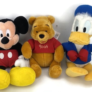 May include: Three plush Disney character toys: Mickey Mouse in red shorts, Winnie the Pooh in a red shirt, and Donald Duck in a blue sailor suit. The toys are soft and colorful, perfect for children.