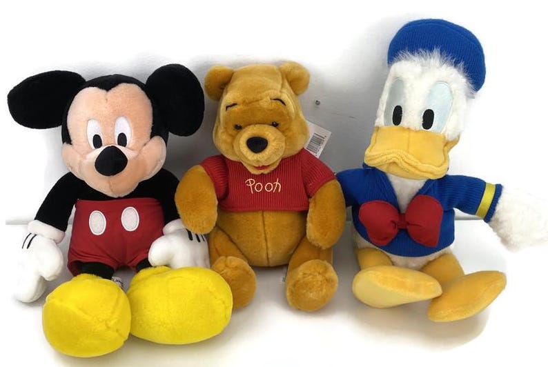 May include: Three plush Disney character toys: Mickey Mouse in red shorts, Winnie the Pooh in a red shirt, and Donald Duck in a blue sailor suit. The toys are soft and colorful, perfect for children.