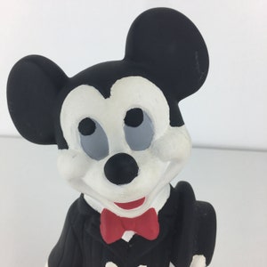Op de afbeelding: Een zwart-witte keramische figuur van Mickey Mouse die een smoking draagt met een rode strik. De figuur staat met zijn hoofd lichtjes naar de zijkant gekanteld.