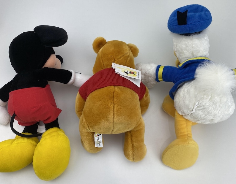 May include: Three plush Disney character toys: Mickey Mouse, Winnie the Pooh, and Donald Duck. Mickey Mouse is in a classic outfit, Winnie the Pooh wears a red shirt, and Donald Duck has a blue sailor hat and jacket.