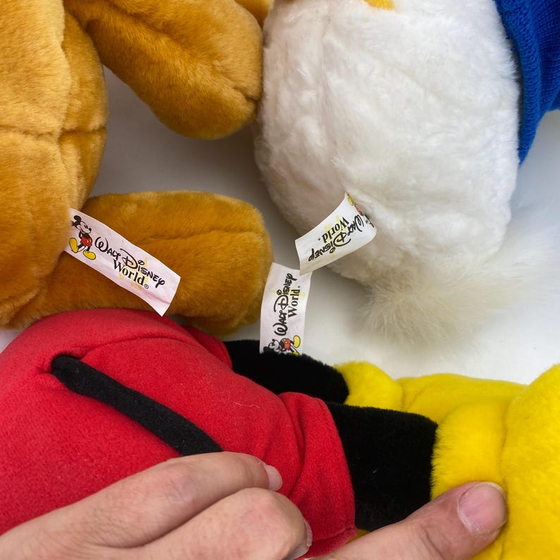 May include: Close-up of several Disney plush toys, including Mickey Mouse, Donald Duck, and a yellow bear. Each toy has a tag that reads "Walt Disney World."