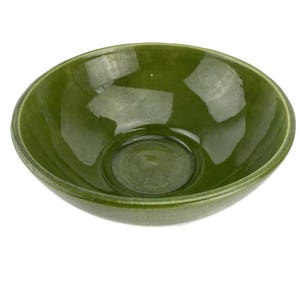 May include: A glossy, olive green ceramic bowl with a rounded shape. The bowl has a wide rim and a slightly textured surface, reflecting light. The interior features a circular indentation at the base. This bowl is suitable for serving food.