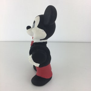 Op de afbeelding: Een zwart-wit rubberen Mickey Mouse-figuur dat een zwart smoking met een rode strik en rode broek draagt.