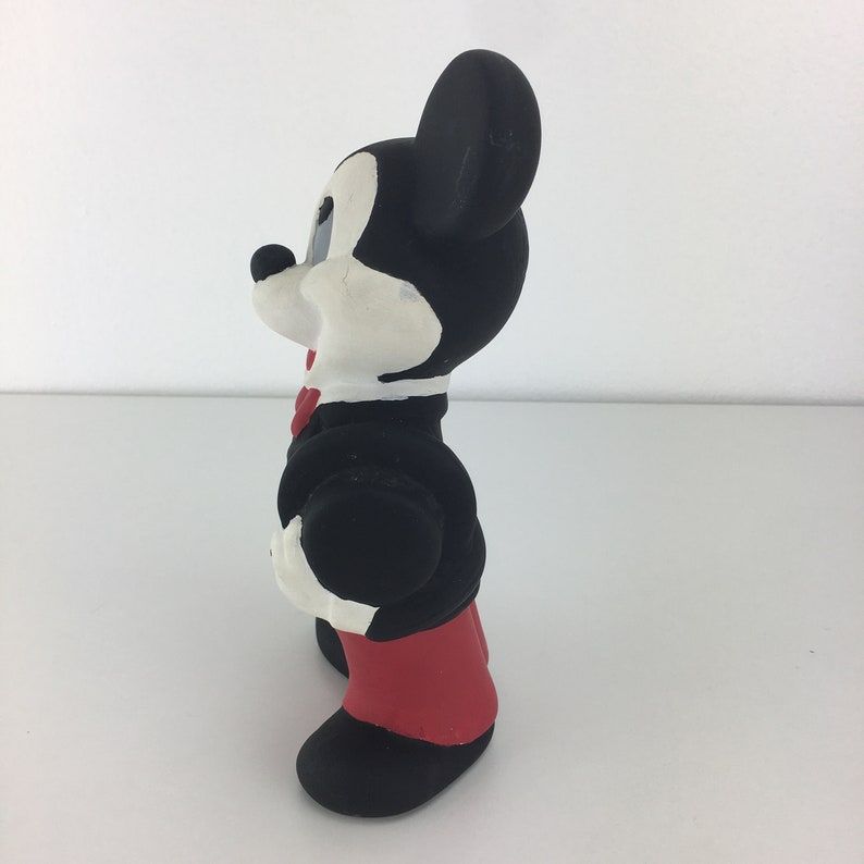 Op de afbeelding: Een zwart-wit rubberen Mickey Mouse-figuur dat een zwart smoking met een rode strik en rode broek draagt.