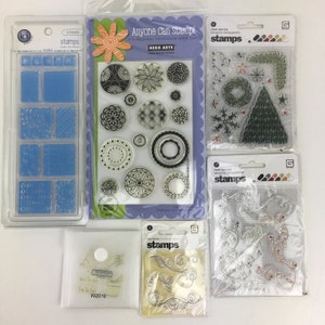 May include: A set of nine clear stamps in a blue and white plastic case. The stamps feature various designs, including geometric shapes, floral patterns, and a checkered pattern. The case has the words "stamps" and "icons" printed on it.