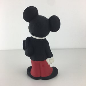 Op de afbeelding: Een zwart-witte keramische figuur van Mickey Mouse, die een zwart pak, een wit overhemd en een rode broek draagt. Hij staat met zijn armen langs zijn zijde en zijn hoofd schuin.