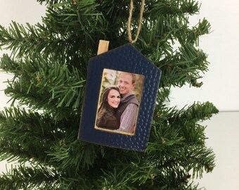 May include: A blue house-shaped Christmas ornament with a gold frame and a photo of a couple inside. The ornament has a rustic, farmhouse style.