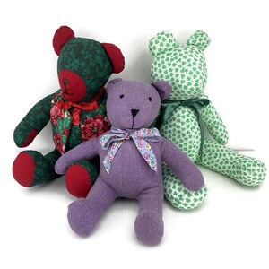 May include: Three handmade teddy bears in various colors and patterns. One is green with red accents and a floral vest, another is purple with a floral bow, and the third is green with white shamrocks and a green bow. These plush toys are perfect for children.
