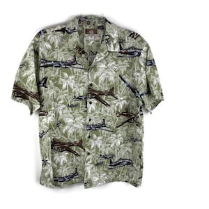 May include: A short-sleeved shirt with a light green base, patterned with aeroplanes and palm trees in brown, grey, and white. The shirt has a classic collar and a button-up front. The design is repeated across the fabric.