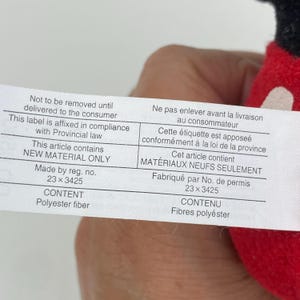 Puede incluir: Una etiqueta blanca con texto negro, que incluye "No debe retirarse hasta la entrega al consumidor" y "MATERIAL NUEVO SOLAMENTE". La etiqueta tambi&eacute;n enumera "Fibra de poli&eacute;ster" como contenido. La etiqueta est&aacute; adherida a una tela roja.