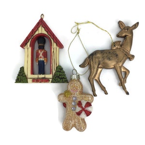 May include: Three vintage Christmas ornaments: a gingerbread man with a candy cane, a gold deer, and a small house with a toy soldier inside.
