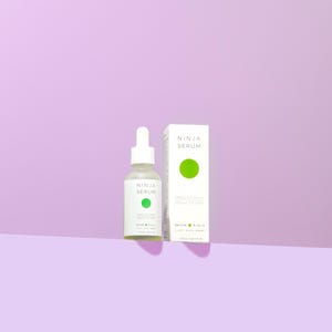 Può includere: Un flacone bianco di siero al tè verde con un contagocce, etichettato "Ninja Serum" e "Green Tea Serum" con un cerchio verde. Il flacone è accanto a una scatola bianca con la stessa etichetta e un cerchio verde.