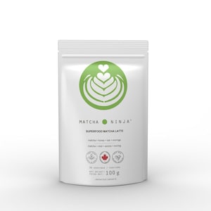 Pu&ograve; includere: Una busta bianca con un logo verde a forma di cuore con un design a spirale. Il testo "MATCHA NINJA SUPERFOOD MATCHA LATTE" &egrave; stampato sulla busta. Gli ingredienti sono elencati come "matcha + honey + oat + moringa" e "matcha + miel + avoine + moringa". La busta contiene 100 grammi di polvere di matcha.