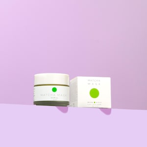 Può includere: Un barattolo bianco con un cerchio verde e il testo "MATCHA MASK" sul davanti. Accanto al barattolo c'è una scatola bianca con il testo "MATCHA MASK" e un cerchio verde sul davanti.