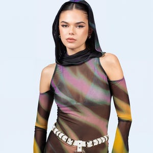 Op de afbeelding: Een doorschijnende jurk met lange mouwen en een capuchon, met een kleurrijk, abstract patroon in bruin, geel, roze en groen. Een witte riem met een zilveren ringgesp accentueert de taille. De jurk heeft uitgesneden schouders.