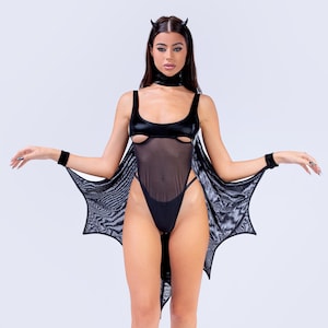 Könnte beinhalten: Schwarzes Teufel-Kostüm mit einem Body mit Ausschnitten, durchsichtigem Mesh und einem Fledermausflügel-Umhang. Inklusive Halsband, Armbändern und Plateau-Heels. Das Kostüm ist aus glänzendem Material gefertigt.