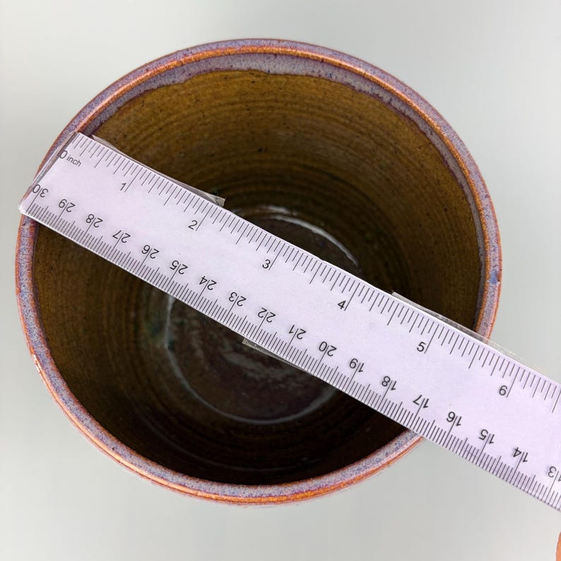 May include: A handmade ceramic pot with a brown interior and a purple and orange rim. A ruler is placed across the top, showing a measurement of approximately 9 inches.