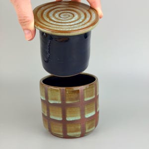 May include: A white ceramic mug with a black handle and the text "But First, Coffee" in a bold, black font. The mug is set against a blurred background, suggesting a cozy setting.