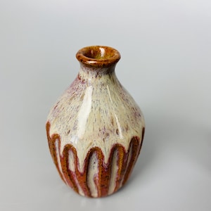 May include: A small, white ceramic vase with a brown rim and a textured, ribbed design. The vase has a drip glaze effect, with white glaze dripping down the brown ribs.