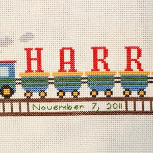 May include: A blue and green train with red letters spelling "HARRY" and the date "November 7, 2011" embroidered on a white background.