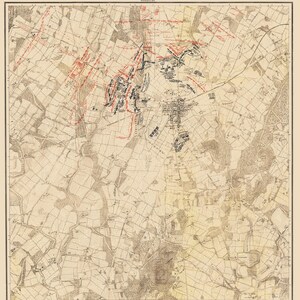 以下が含まれることがあります： 1876年付の「Map of the Battle Field of Gettysburg」と題された歴史的な地図。ベージュ色の地図には、黒い地形線、グリッド座標、そして初日の戦闘における軍隊の配置を示す赤と黒のマーキングが描かれています。