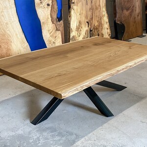 Peut inclure: Une grande table basse en bois naturel avec un bord brut et des pieds en X en métal noir. Le plateau de la table a un design à bord brut, avec la forme naturelle du bois préservée.