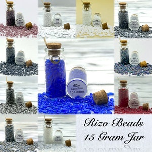 May include: Assortment of 15 gram jars of glass seed beads in various colors, including amethyst, white, jet hematite, sapphire, purple iris, and red. Each jar has a cork stopper and a label with the bead color and weight.