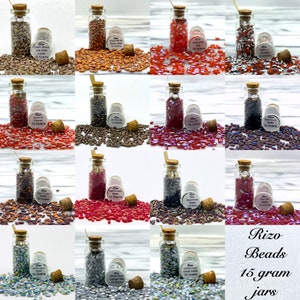 May include: Assortment of 15 gram jars filled with various colors of glass beads. The jars have cork tops and are arranged in a grid pattern. The beads are oval shaped and have a matte finish. The text on the jars reads "Rizo Beads 15 gram jars".