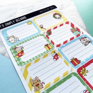 May include: Sheet of Christmas-themed gift tags with cartoon cats. Each tag has a rectangular shape with a colored border and lined interior for writing. The tags feature various festive designs, including a star, candy cane, gift boxes, and a Christmas stocking.