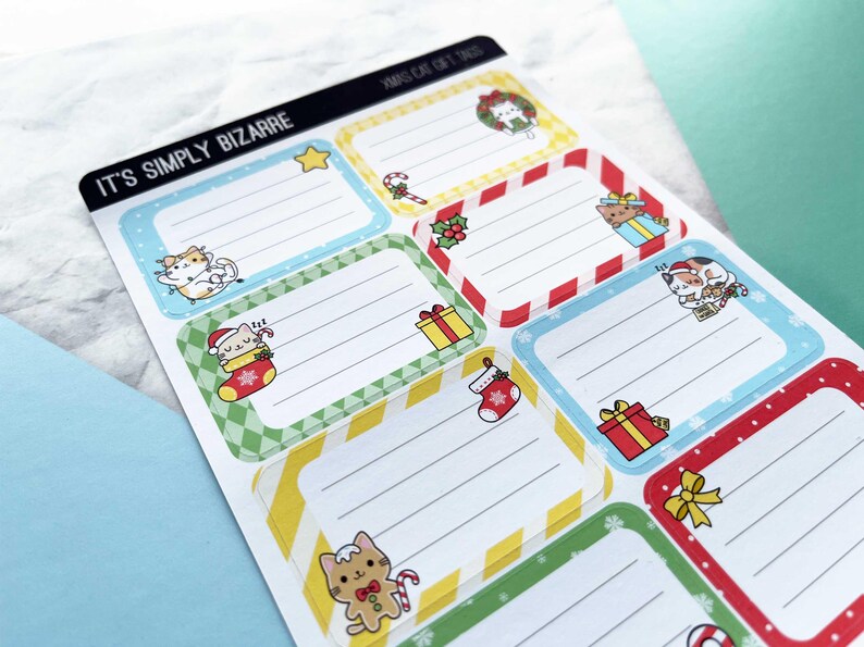 May include: Sheet of Christmas-themed gift tags with cartoon cats. Each tag has a rectangular shape with a colored border and lined interior for writing. The tags feature various festive designs, including a star, candy cane, gift boxes, and a Christmas stocking.