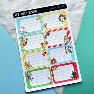 May include: Sheet of Christmas cat gift tags with various designs. Each tag features a rectangular frame with a different color border and a cartoon cat illustration. The tags include text that reads "IT'S SIMPLY BIZARRE" and "XMAS CAT GIFT TAGS".