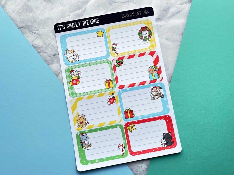 May include: Sheet of Christmas cat gift tags with various designs. Each tag features a rectangular frame with a different color border and a cartoon cat illustration. The tags include text that reads "IT'S SIMPLY BIZARRE" and "XMAS CAT GIFT TAGS".